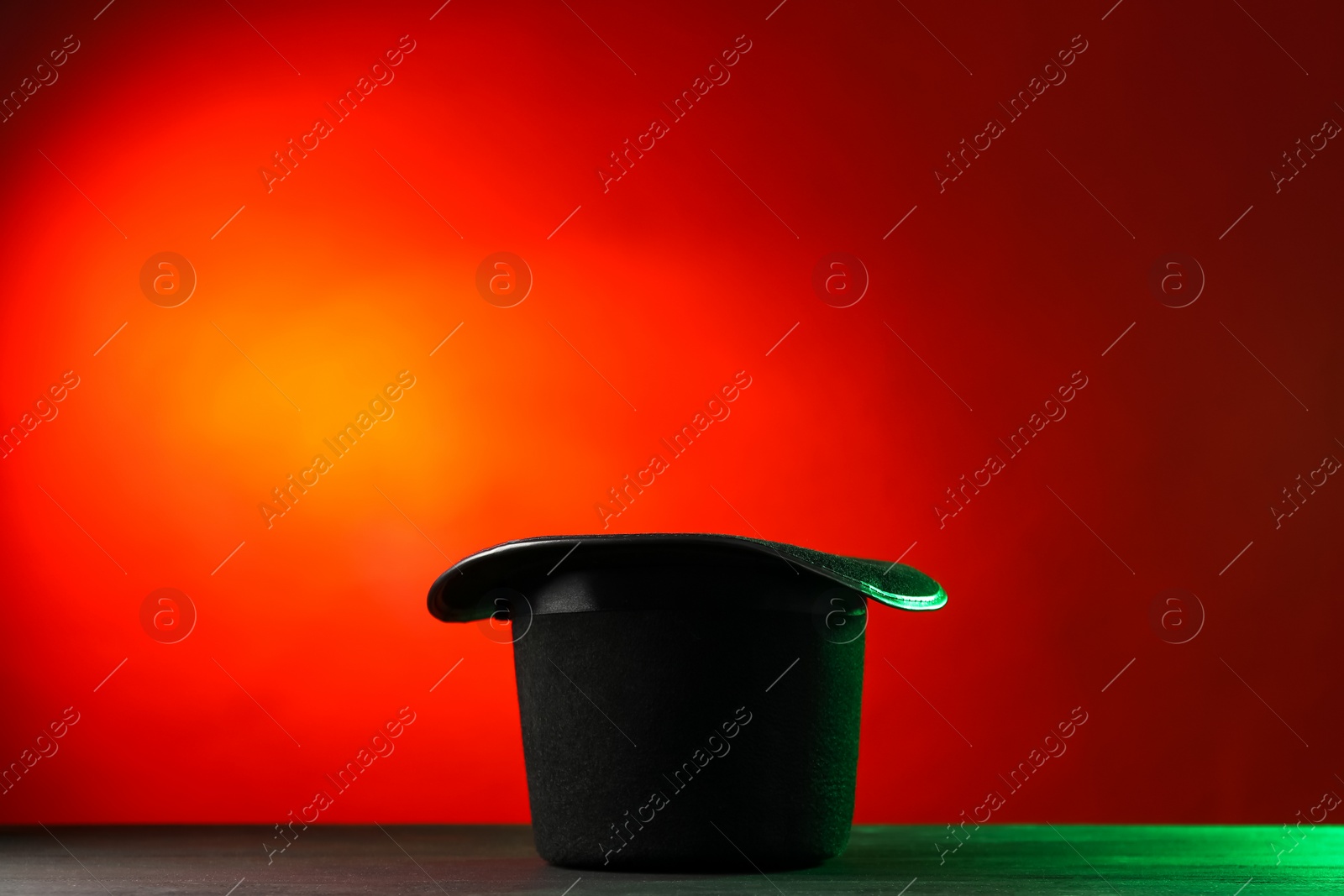 Photo of Magician's hat on black wooden table against color background, space for text