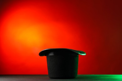 Photo of Magician's hat on black wooden table against color background, space for text