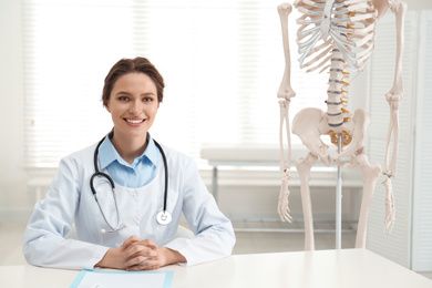 Female orthopedist at table near human skeleton model in office