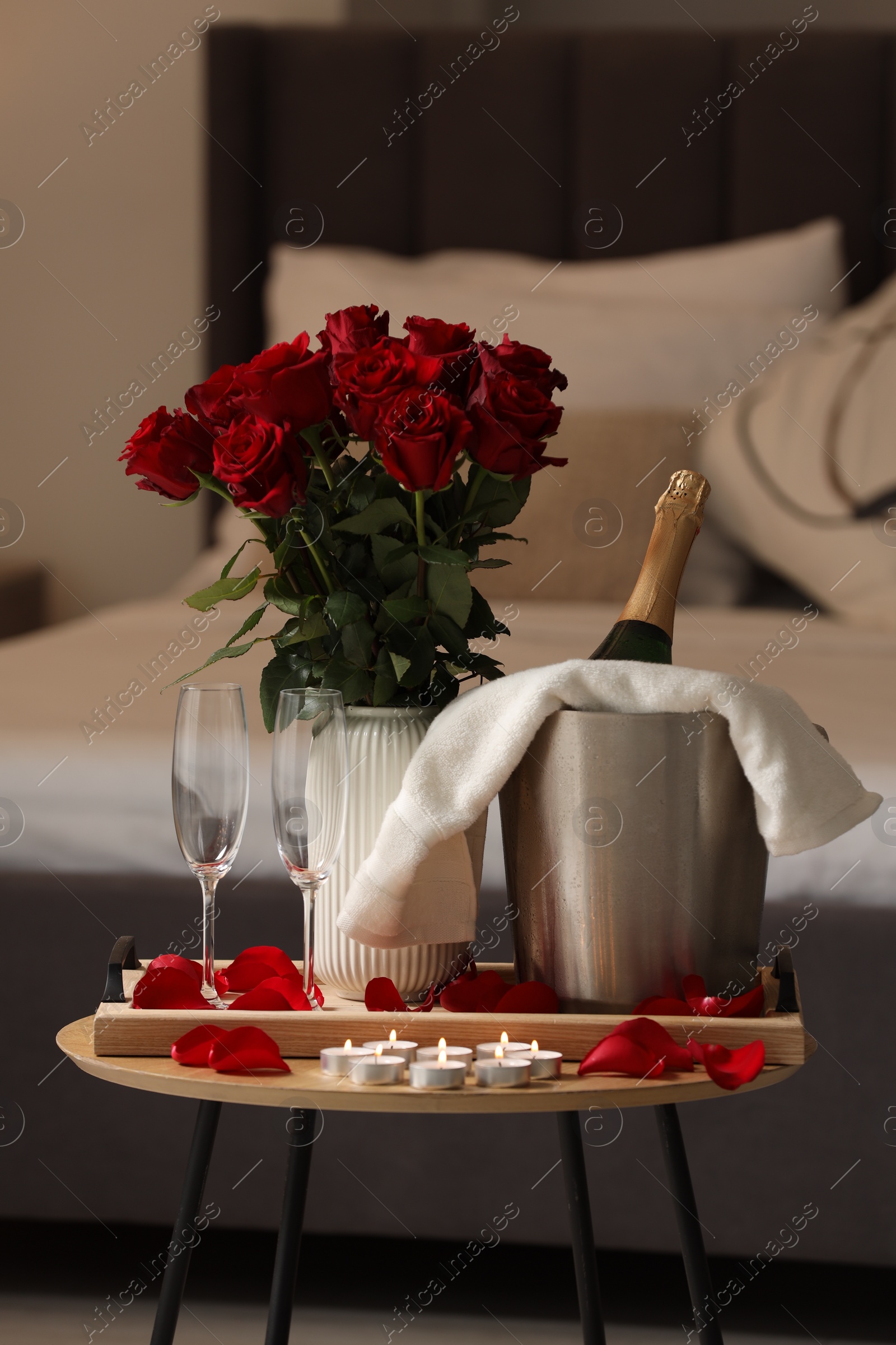 Photo of Honeymoon. Sparkling wine, glasses and bouquet of roses on wooden table in room