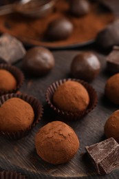 Photo of Delicious chocolate truffles powdered with cocoa on wooden board, closeup