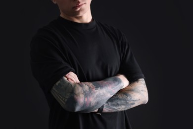 Photo of Young man with tattoos on black background, closeup