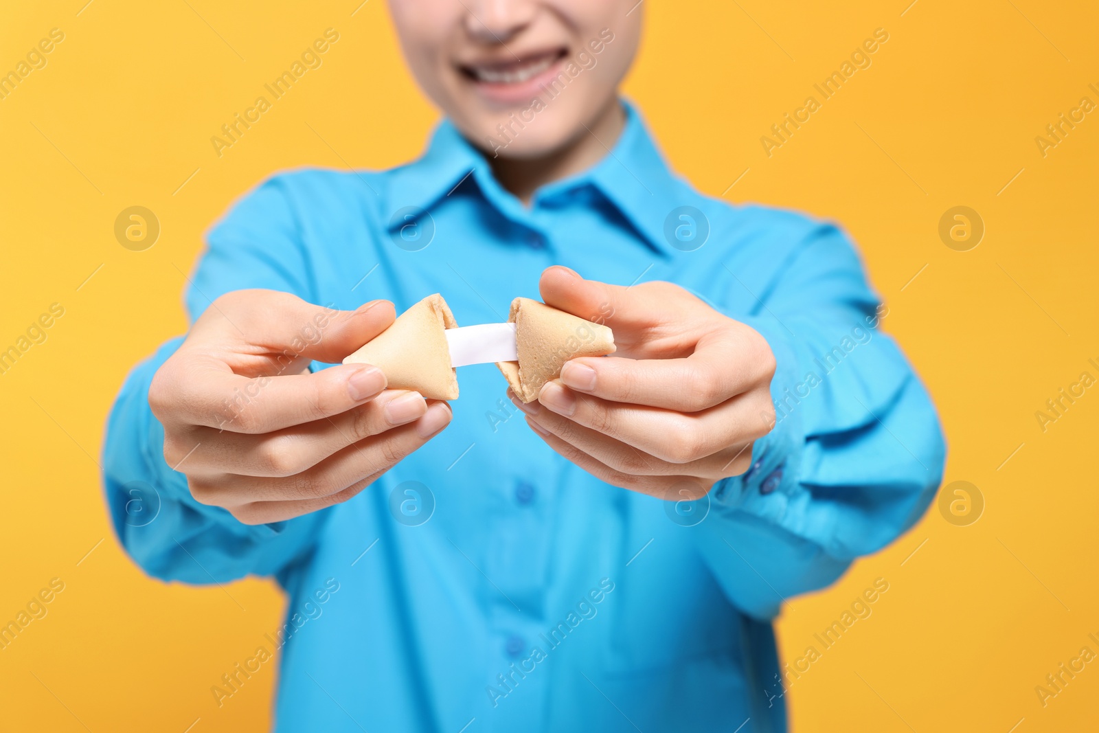 Photo of Young woman holding tasty fortune cookie with prediction on yellow background, closeup