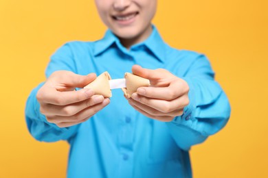 Young woman holding tasty fortune cookie with prediction on yellow background, closeup