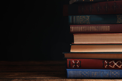 Collection of different books on wooden table against dark background. Space for text