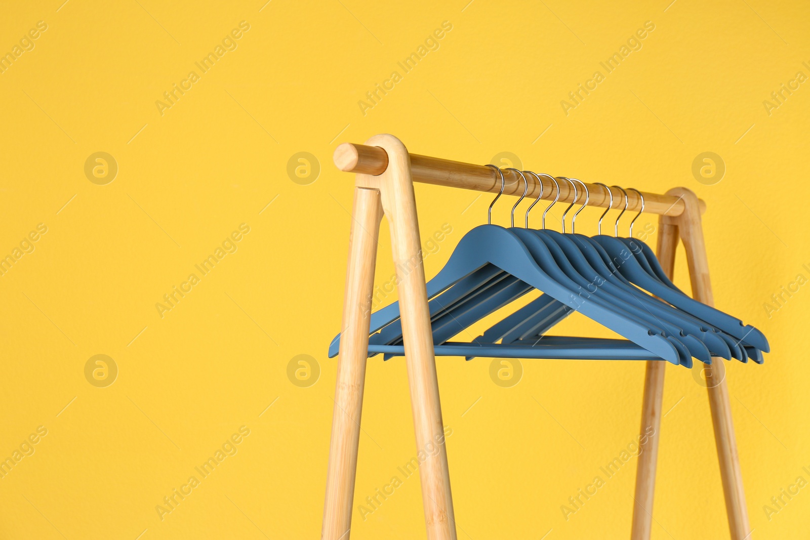 Photo of Wooden rack with clothes hangers on color background, space for text