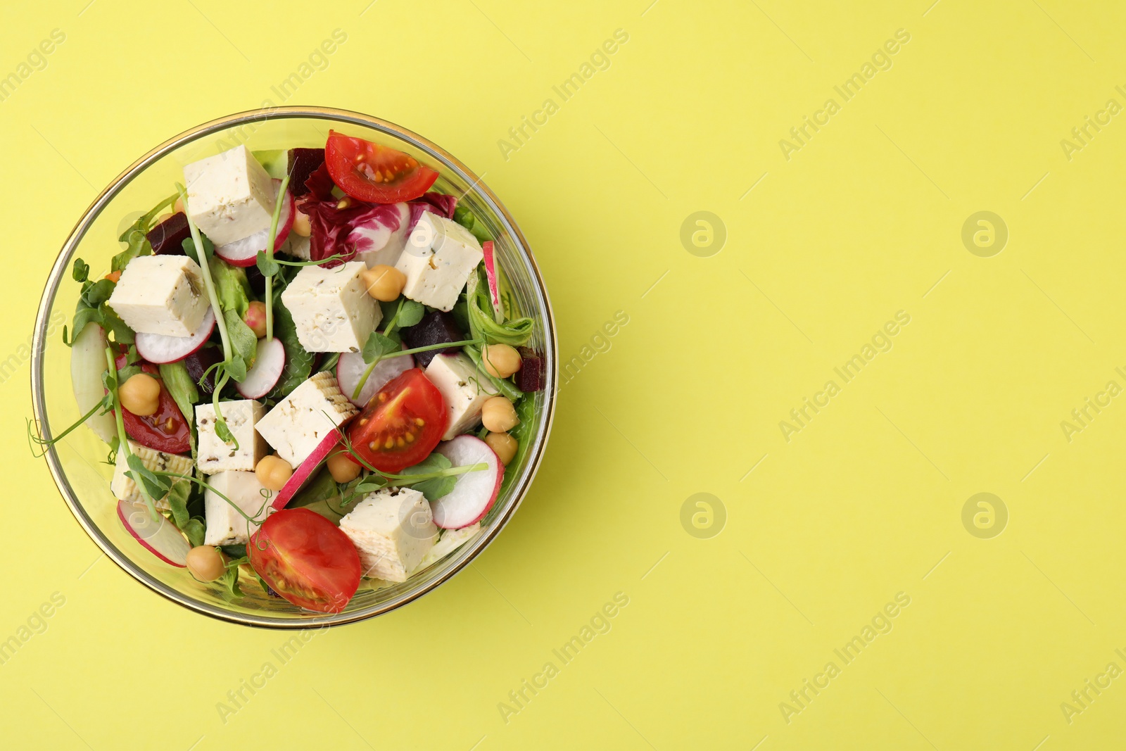 Photo of Bowl of tasty salad with tofu and vegetables on yellow background, top view. Space for text