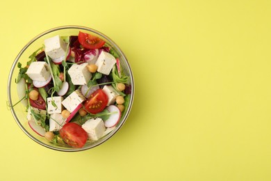 Bowl of tasty salad with tofu and vegetables on yellow background, top view. Space for text