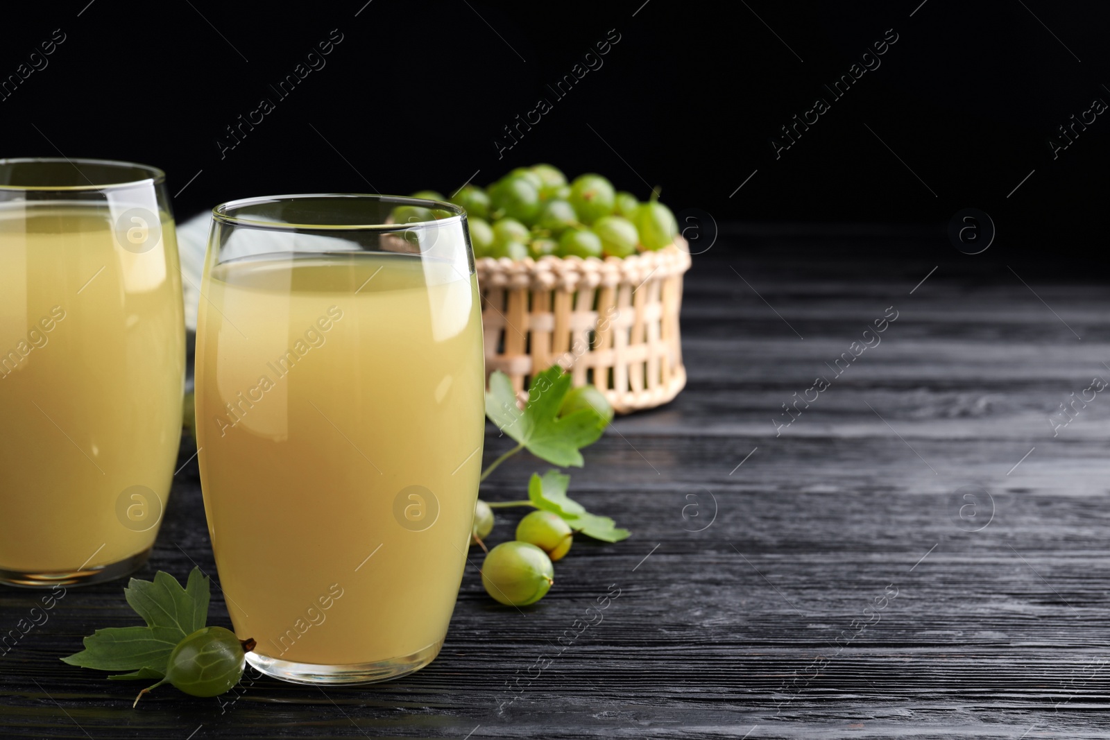 Photo of Tasty gooseberry juice on black wooden table. Space for text
