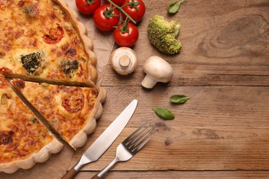 Delicious homemade vegetable quiche, ingredients and cutlery on wooden table, flat lay. Space for text