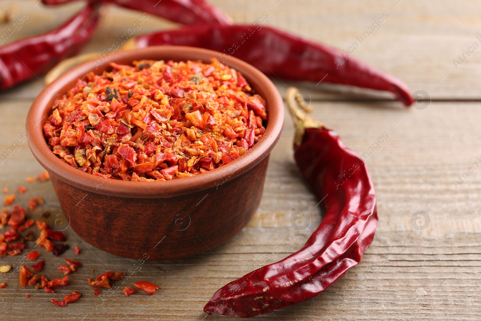 Photo of Aromatic spice. Red chili pepper flakes in bowl and pods on wooden table, closeup. Space for text