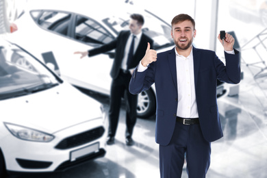 Image of Happy salesman with key in car salon
