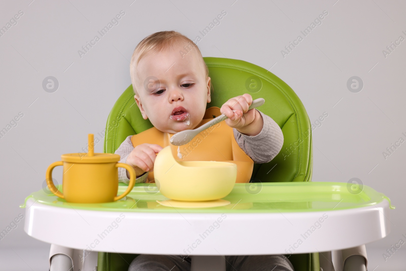Photo of Cute little baby eating healthy food in high chair on gray background