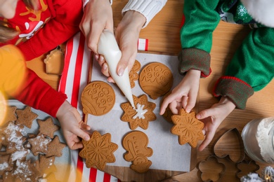 Mother and her little children decorating tasty Christmas cookies at wooden table, top view