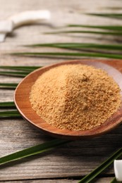 Photo of Spoon with coconut sugar and palm leaves on wooden table, closeup