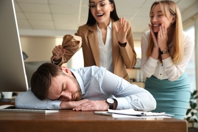 Photo of Young women popping paper bag their behind sleeping colleague in office. Funny joke