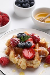 Photo of Delicious Belgian waffle with fresh berries and honey on white table, closeup