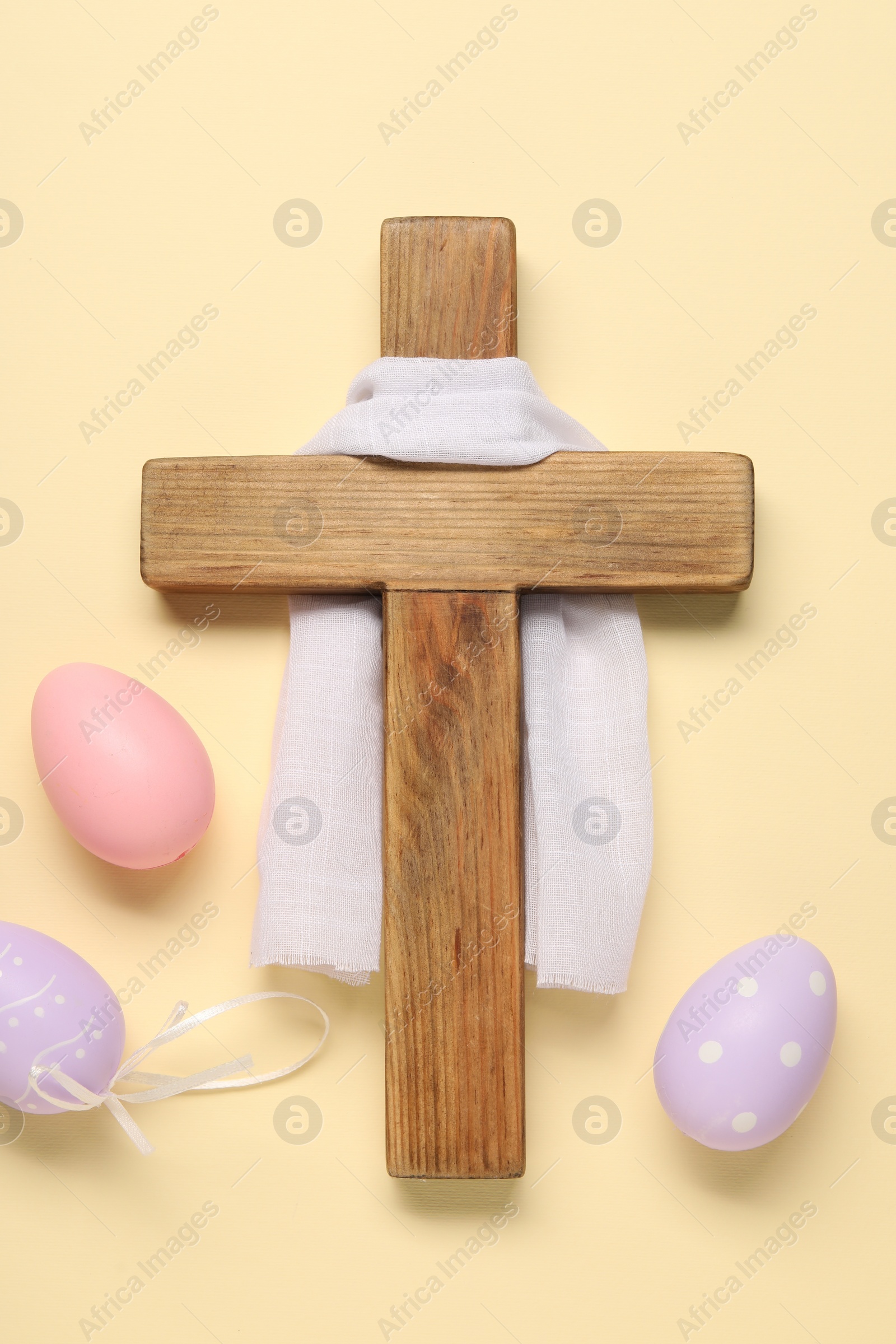 Photo of Wooden cross, white cloth and painted Easter eggs on beige background, flat lay