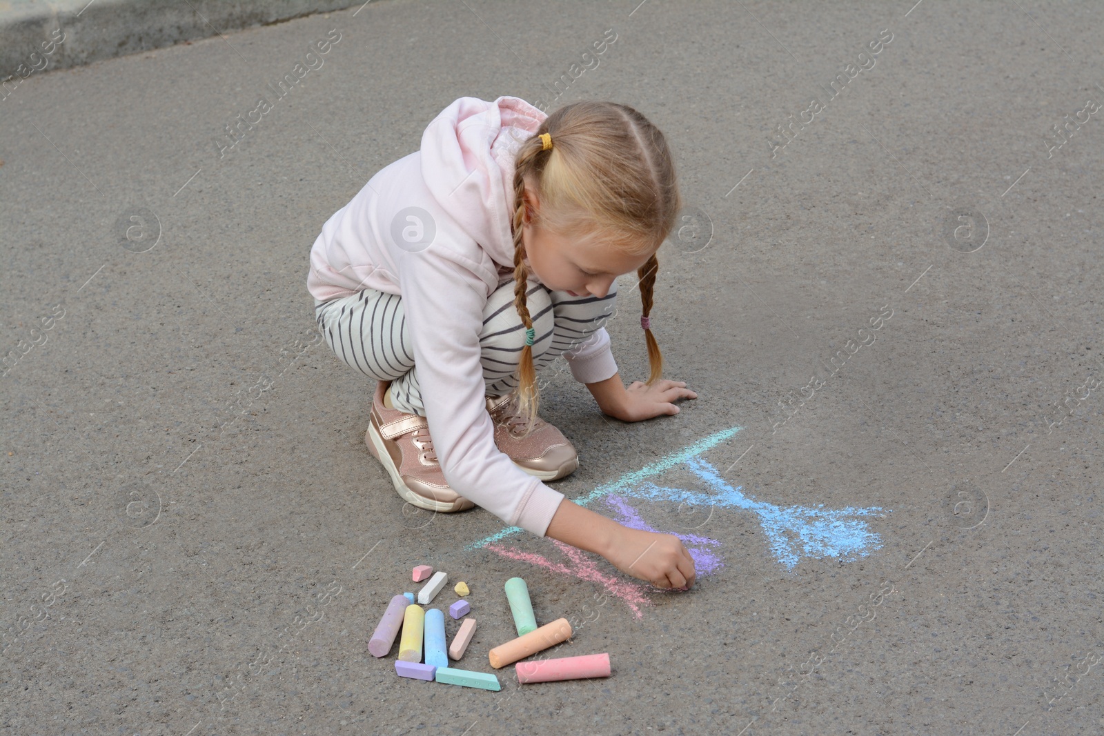 Photo of Little child drawing happy family with chalk on asphalt