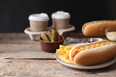 Delicious hot dog with mustard and French fries on wooden table, closeup. Space for text