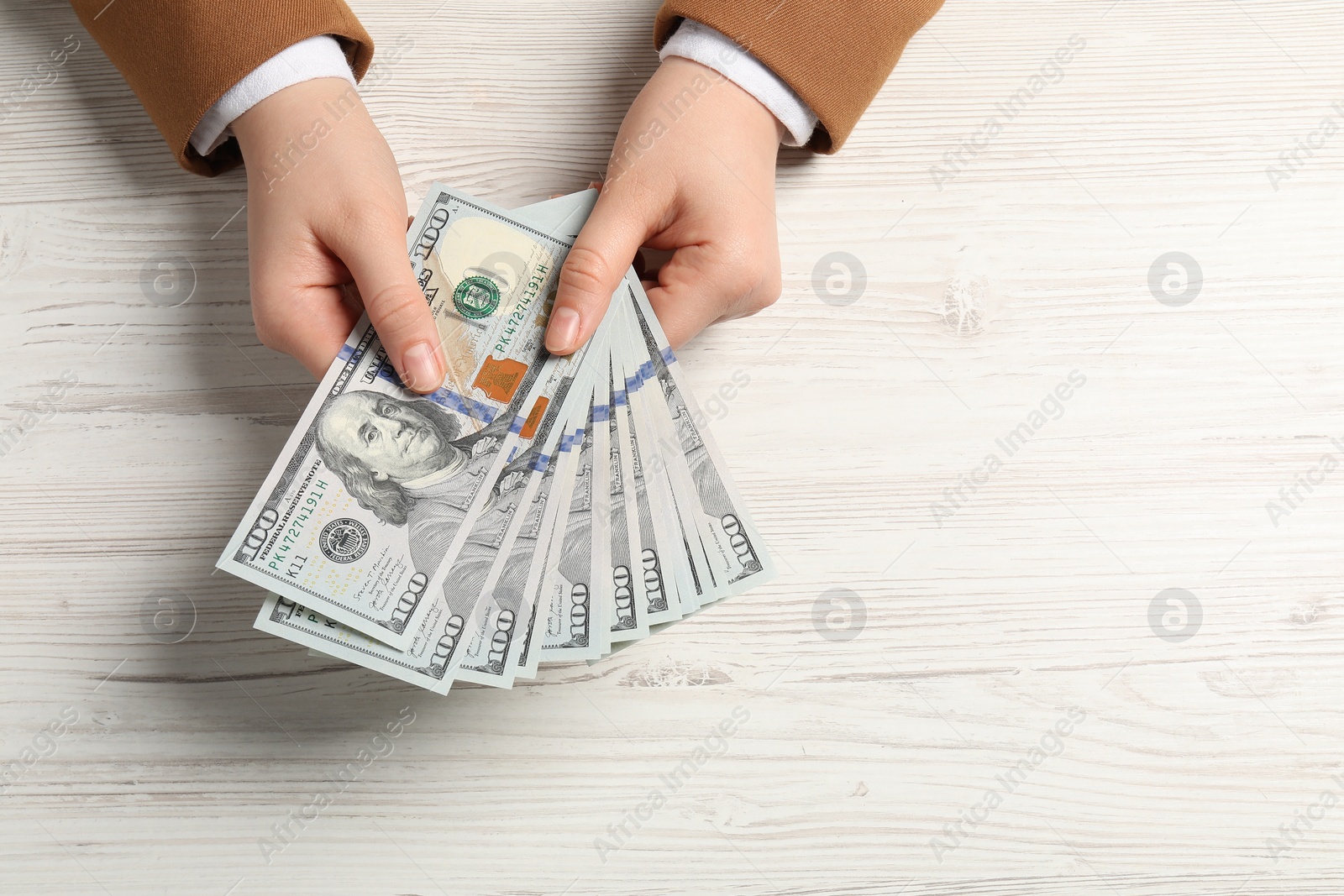 Photo of Money exchange. Woman holding dollar banknotes at white wooden table, top view. Space for text