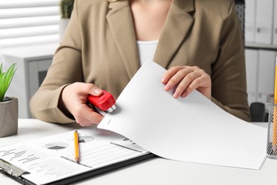 Woman stapling papers at white table indoors, closeup