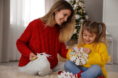 Photo of Happy mother and daughter making paper snowflakes near Christmas tree at home