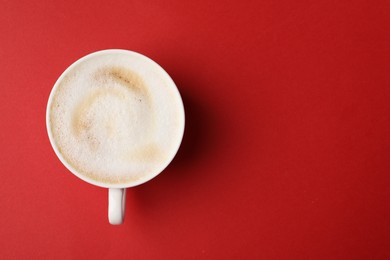 Tasty cappuccino in coffee cup on red background, top view. Space for text