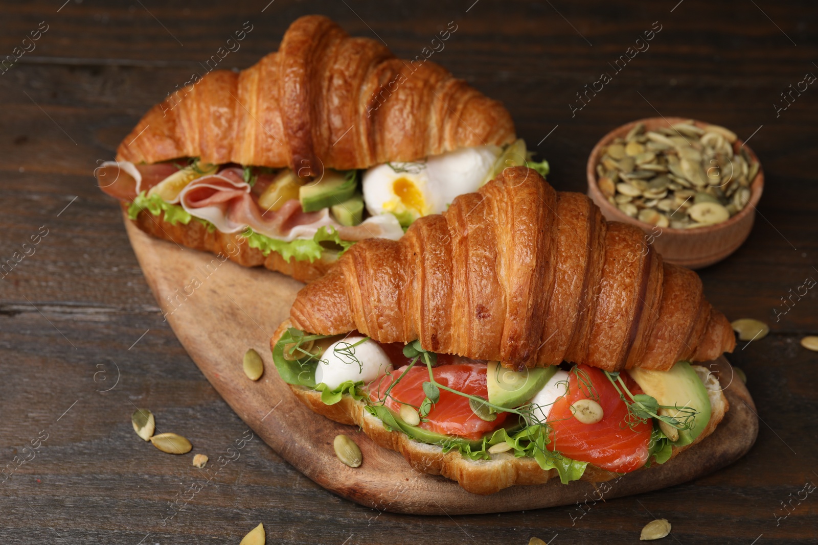 Photo of Delicious croissants with salmon and pumpkin seeds on wooden table