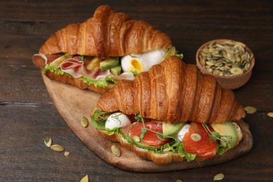 Delicious croissants with salmon and pumpkin seeds on wooden table