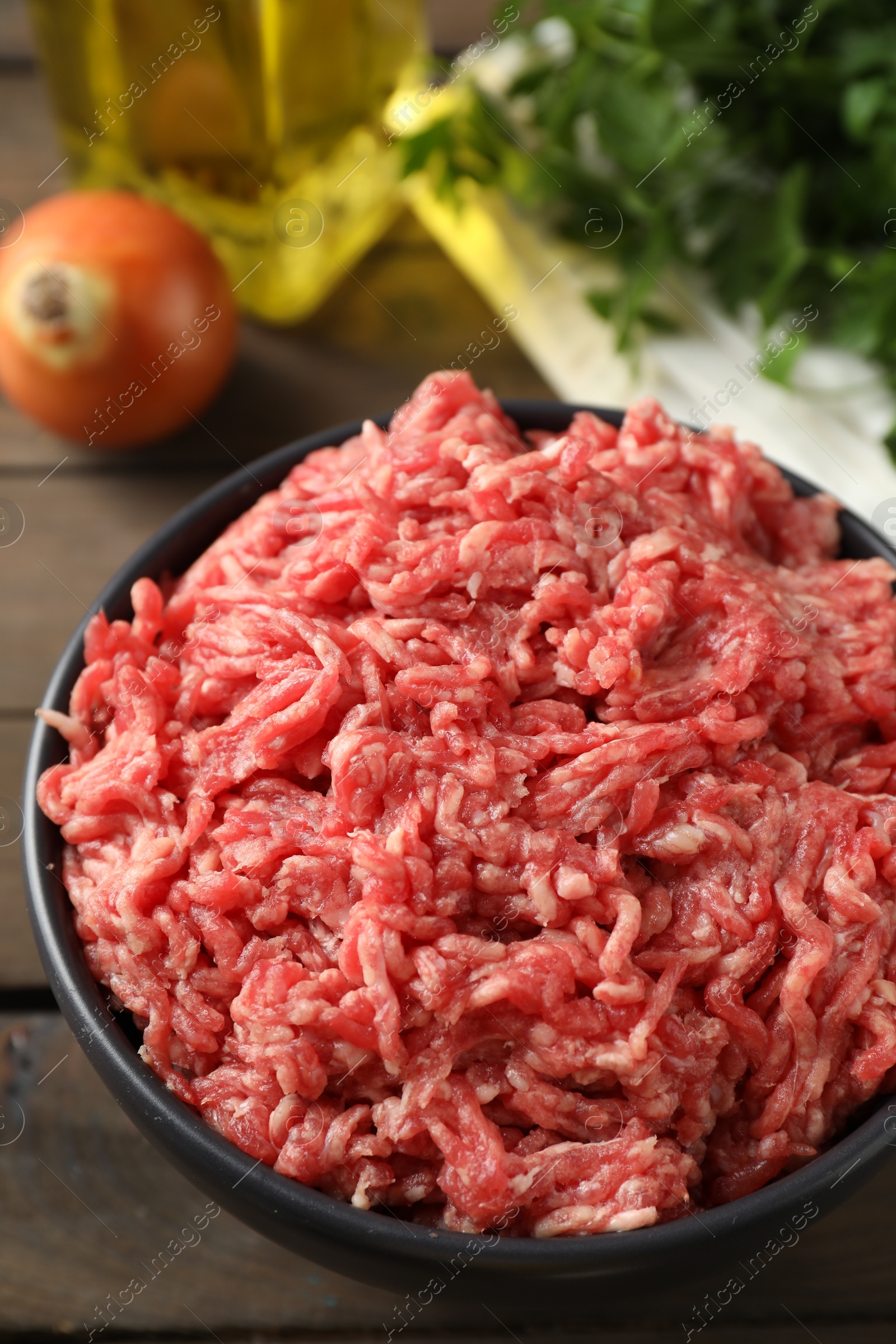 Photo of Raw ground meat in bowl on wooden table, closeup