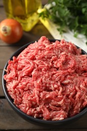 Raw ground meat in bowl on wooden table, closeup