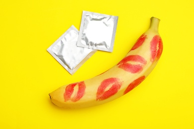 Photo of Condoms and banana with lipstick kiss marks on yellow background, flat lay. Safe sex