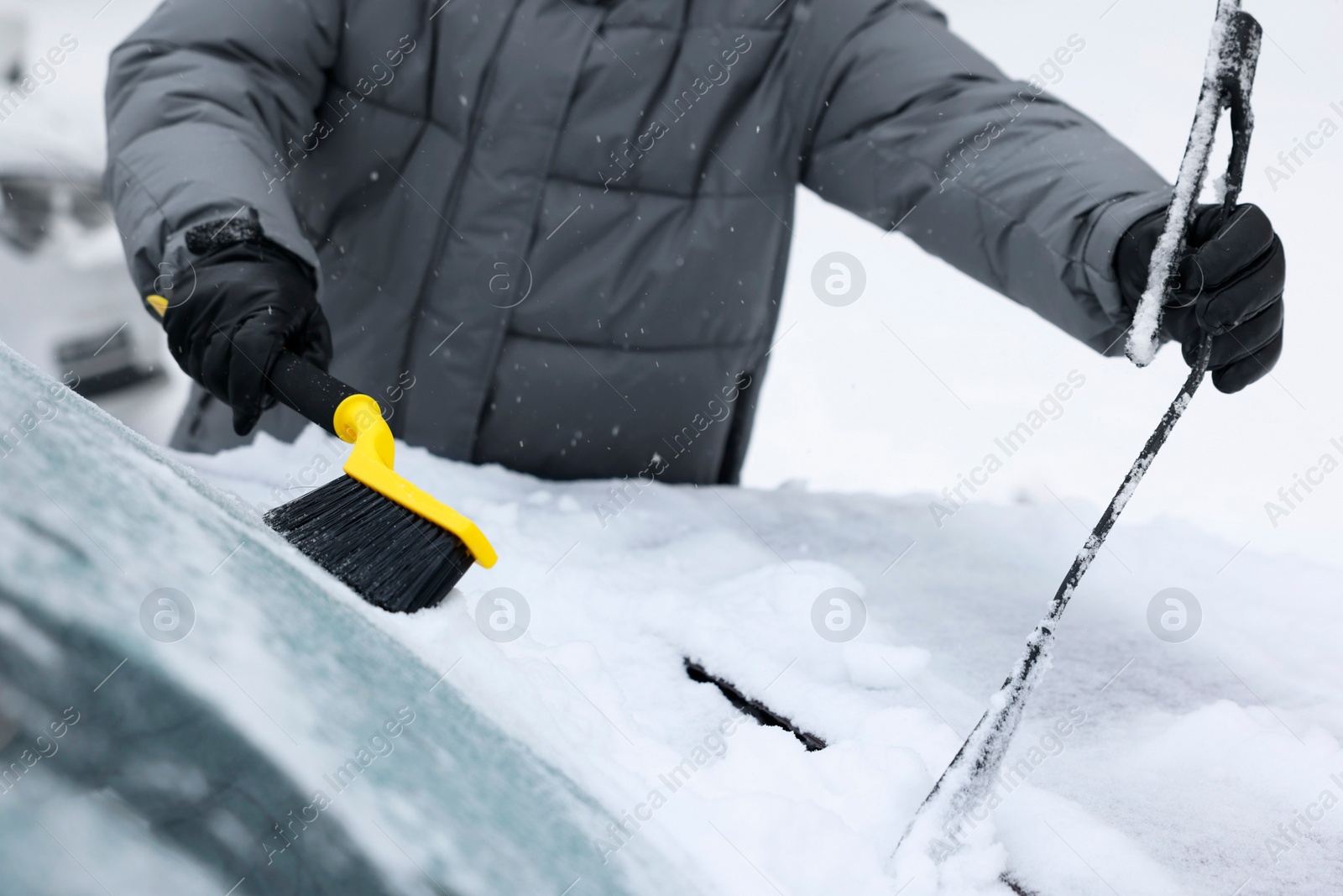 Photo of Man cleaning snow from car windshield outdoors, closeup