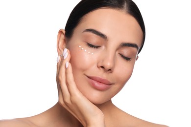 Beautiful young woman with cream on skin under eye against white background