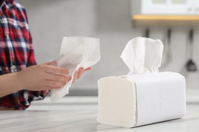 Woman wiping glass with paper towel at white marble table in kitchen, selective focus. Space for text