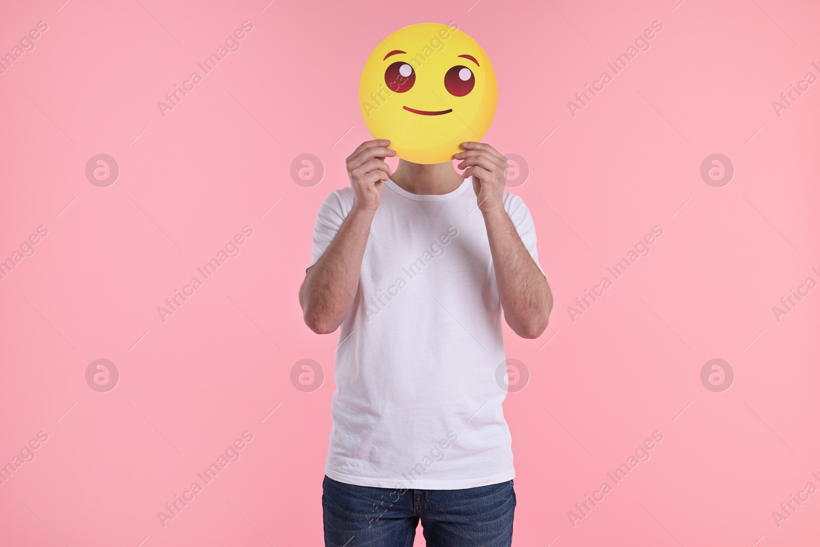 Photo of Man covering face with smiling emoticon on pink background