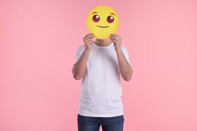 Photo of Man covering face with smiling emoticon on pink background