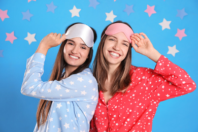 Photo of Beautiful women wearing sleeping masks on light blue background. Bedtime