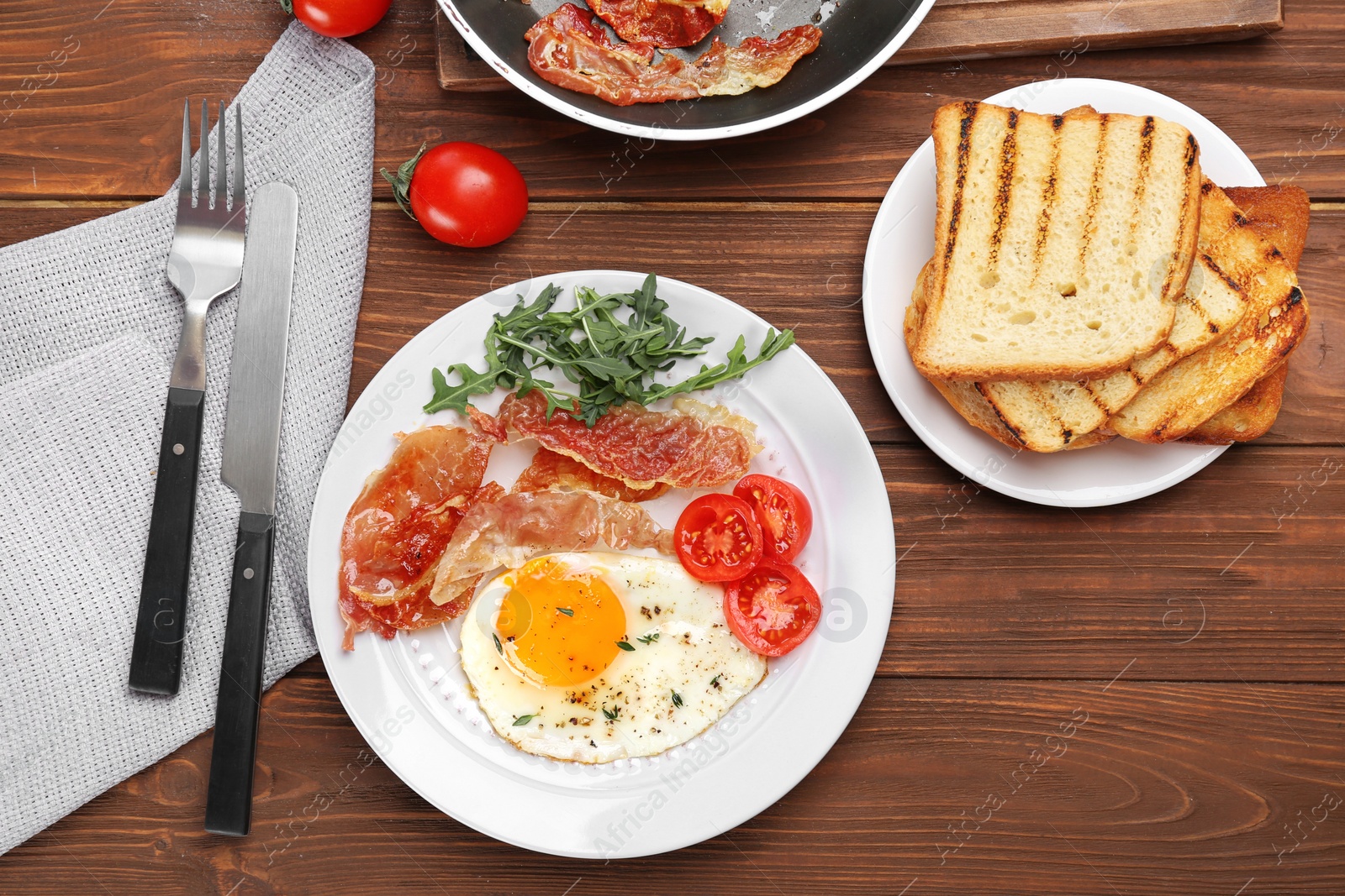 Photo of Plate with fried egg, bacon and tomatoes on wooden background