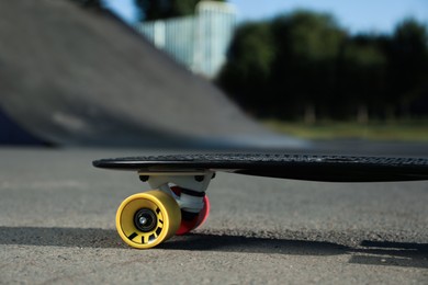 Photo of Modern black skateboard with colorful wheels on asphalt road outdoors, closeup