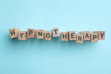 Wooden blocks with word HYPNOTHERAPY on light blue background, flat lay