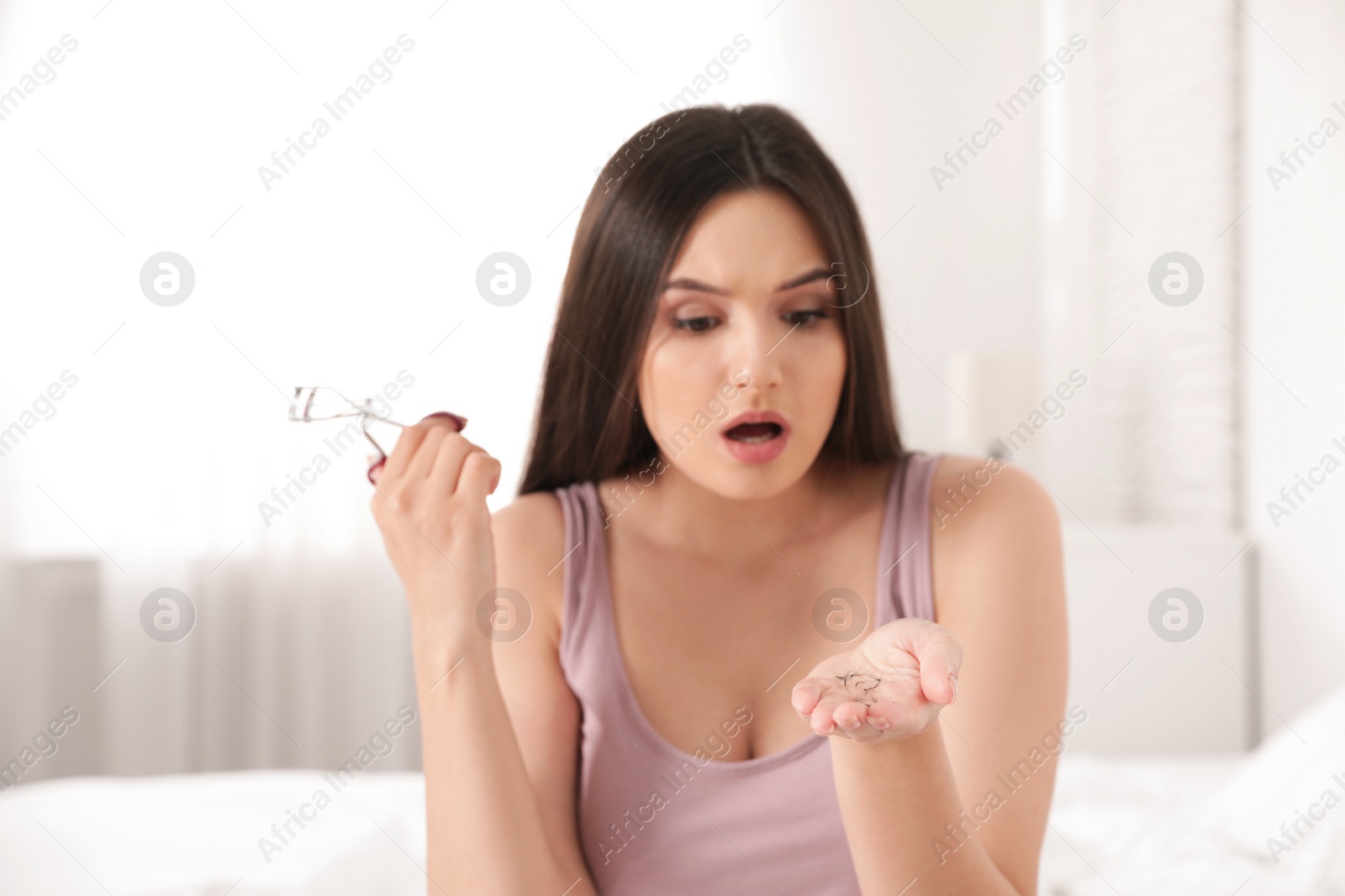 Photo of Beautiful woman holding fallen eyelashes and curler indoors