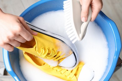 Photo of Woman cleaning stylish sneakers with brush in wash basin, top view