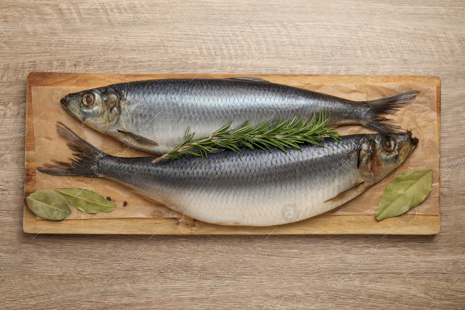 Photo of Board with salted herrings and bay leaves on wooden table, top view