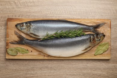 Photo of Board with salted herrings and bay leaves on wooden table, top view