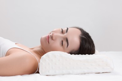 Woman sleeping on orthopedic pillow against light grey background