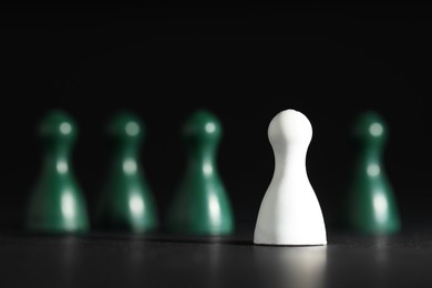 Photo of Choice concept. White pawn in front of green ones on black table, selective focus