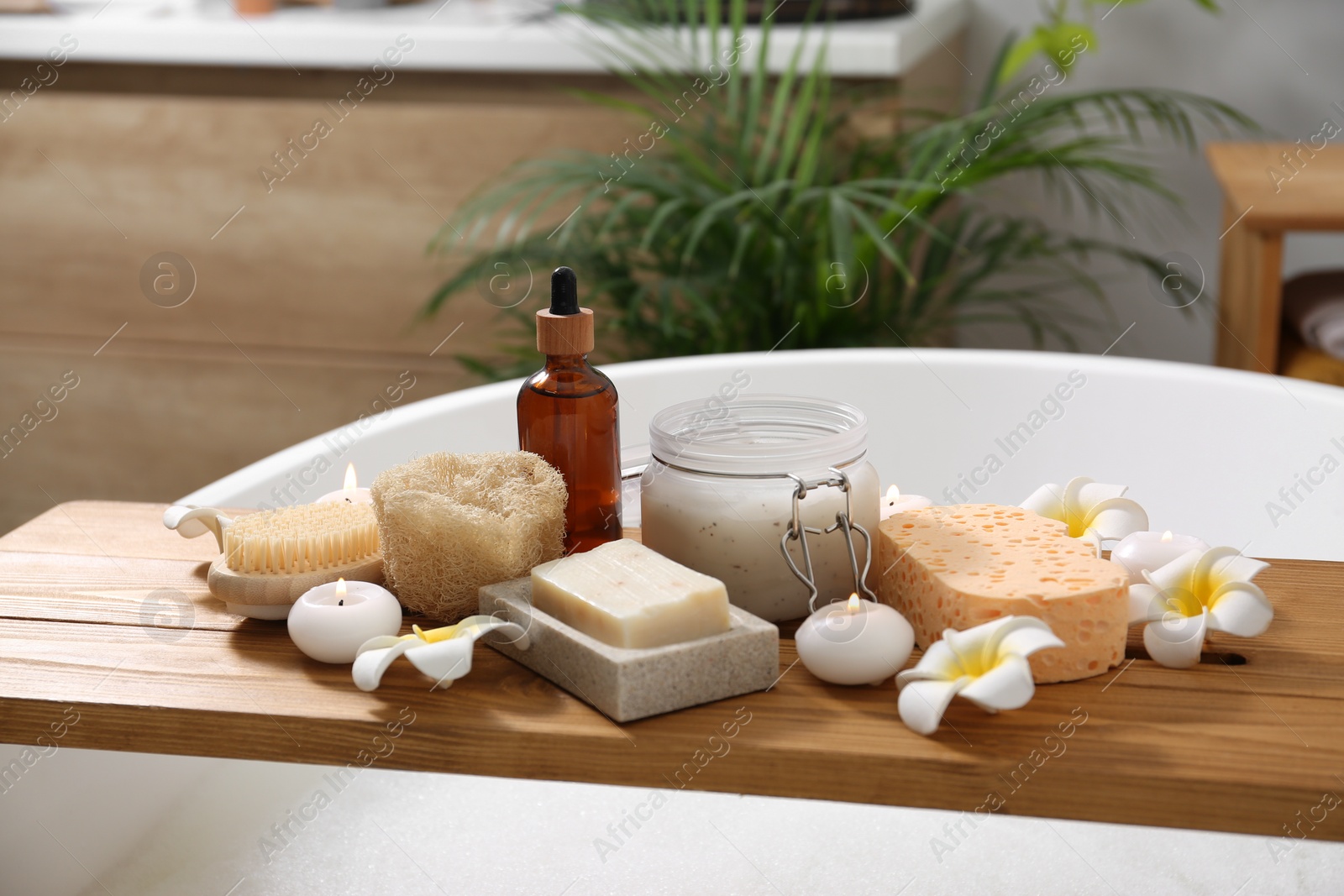 Photo of Composition with different spa products and beautiful flowers on tub tray in bathroom