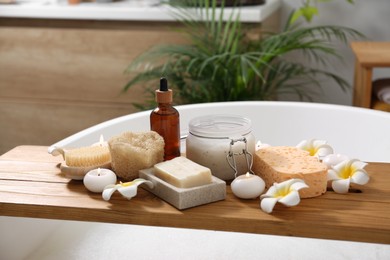 Photo of Composition with different spa products and beautiful flowers on tub tray in bathroom